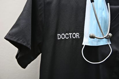 A Doctor's scrubs, stethoscope and face mask. Health workers fighting the Coronavirus (covid-19) with limited personal protective clothing concept.